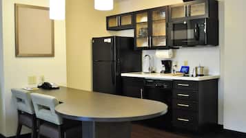 Cocina compacta con refrigerador, microondas y cafetera. Cuenta con una mesa de comedor con sillas y una pequeña isla.