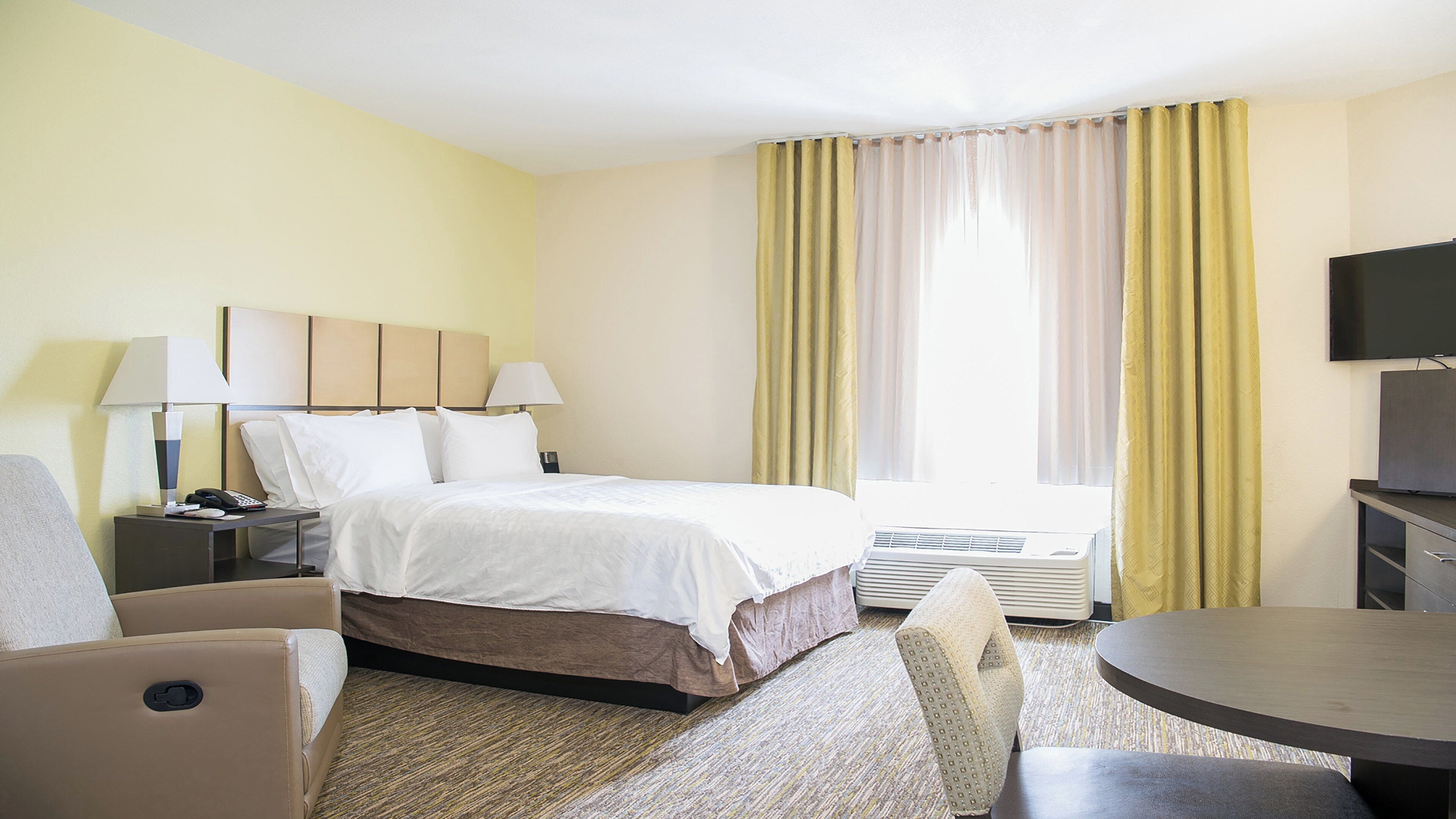 Ein Hotelzimmer mit Bett, Nachttischen, einer Lampe, einem Fernseher, einem Sessel und einem kleinen Tisch.
