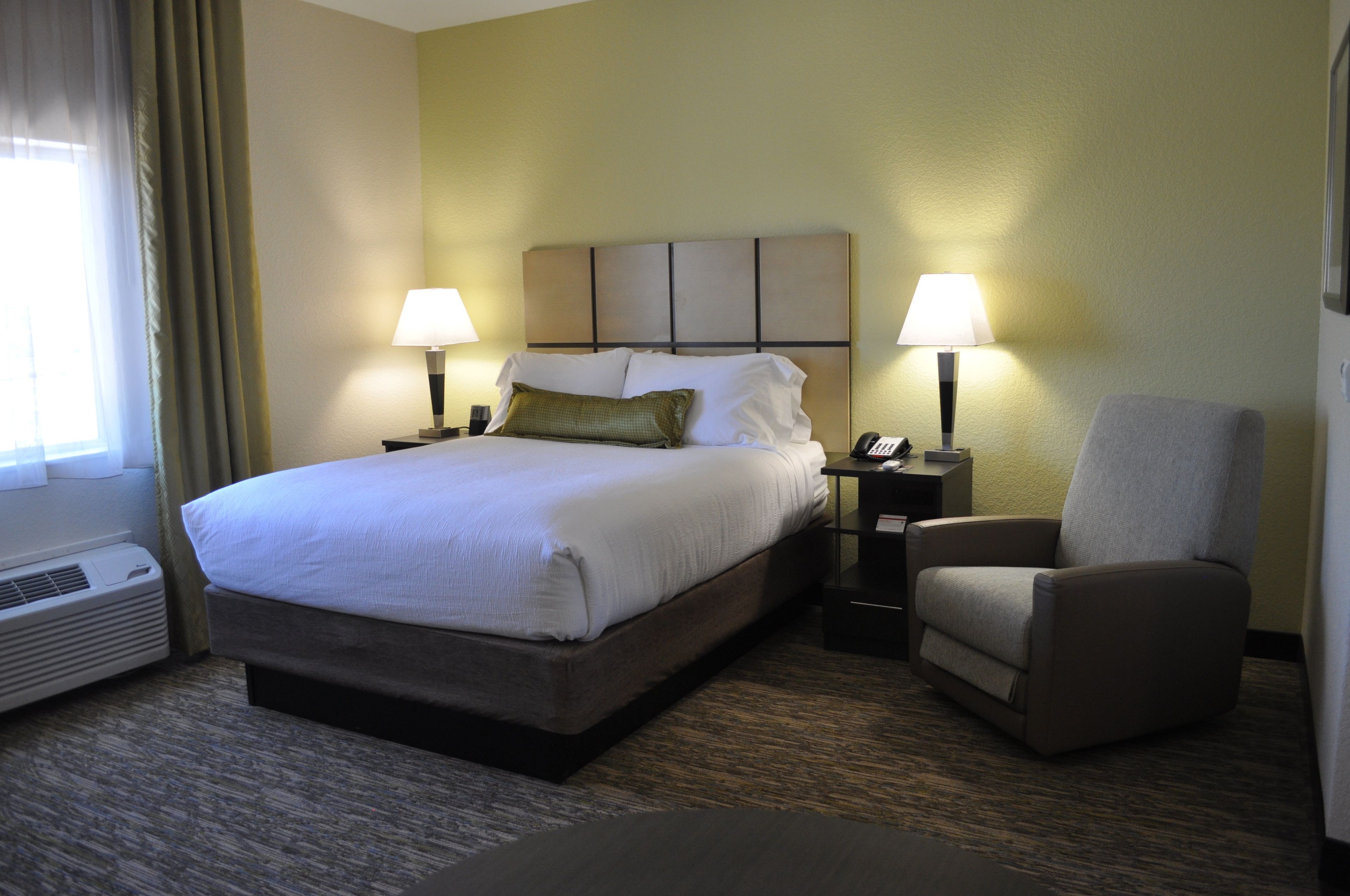 A hotel room with a large bed, two bedside tables with lamps, a chair, and a window with curtains.
