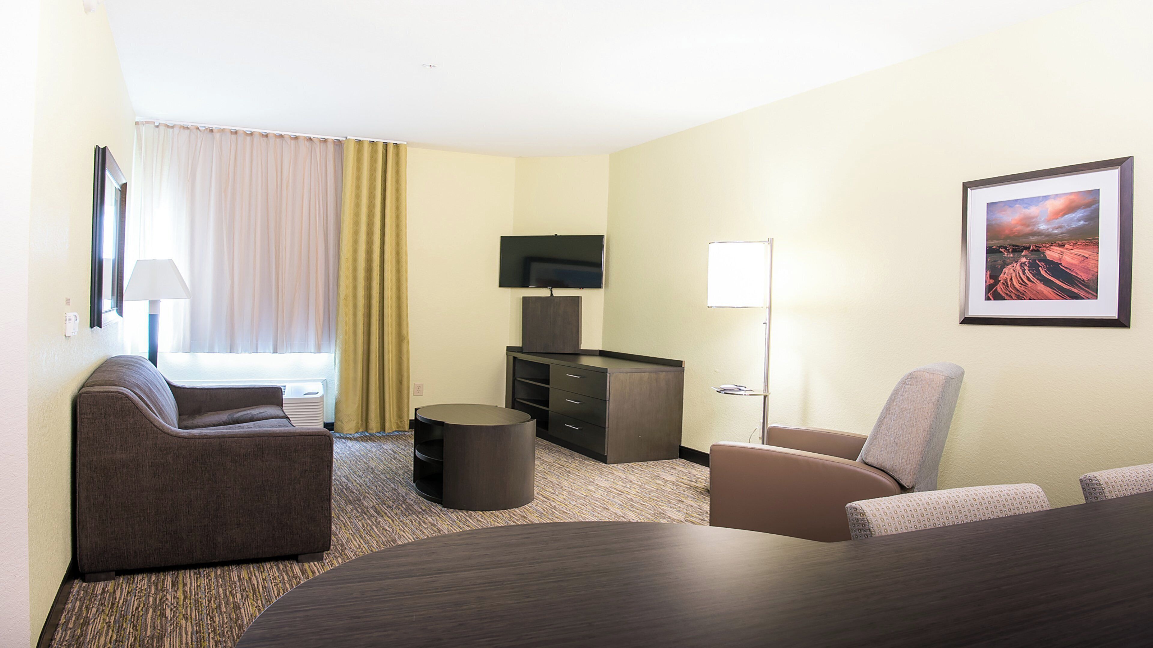 A hotel room with a sofa, armchair, a small table, a television, and a painting on the wall.