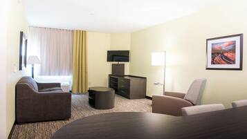 A hotel room with a sofa, armchair, a small table, a television, and a painting on the wall.