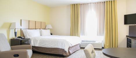 Habitación de hotel con cama, mesitas de noche, escritorio, silla, televisor y ventana con cortinas.