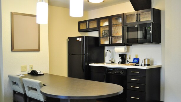 A compact kitchen with a refrigerator, microwave, and coffee maker. There is a small dining area with two chairs and a table. - Candlewood Suites Bay City by IHG (Bay City)