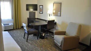 A hotel room with a bed, a desk with a chair, a sofa, a TV, a lamp, and a picture on the wall. - Candlewood Suites Bay City by IHG (Bay City)