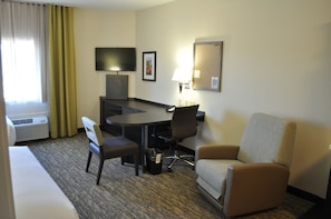 Habitación de hotel con cama, escritorio con silla, sofá, televisor, lámpara y un cuadro en la pared.
