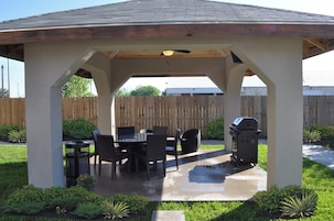 Un patio cubierto con mesa y sillas, una parrilla y una cerca de madera al fondo.