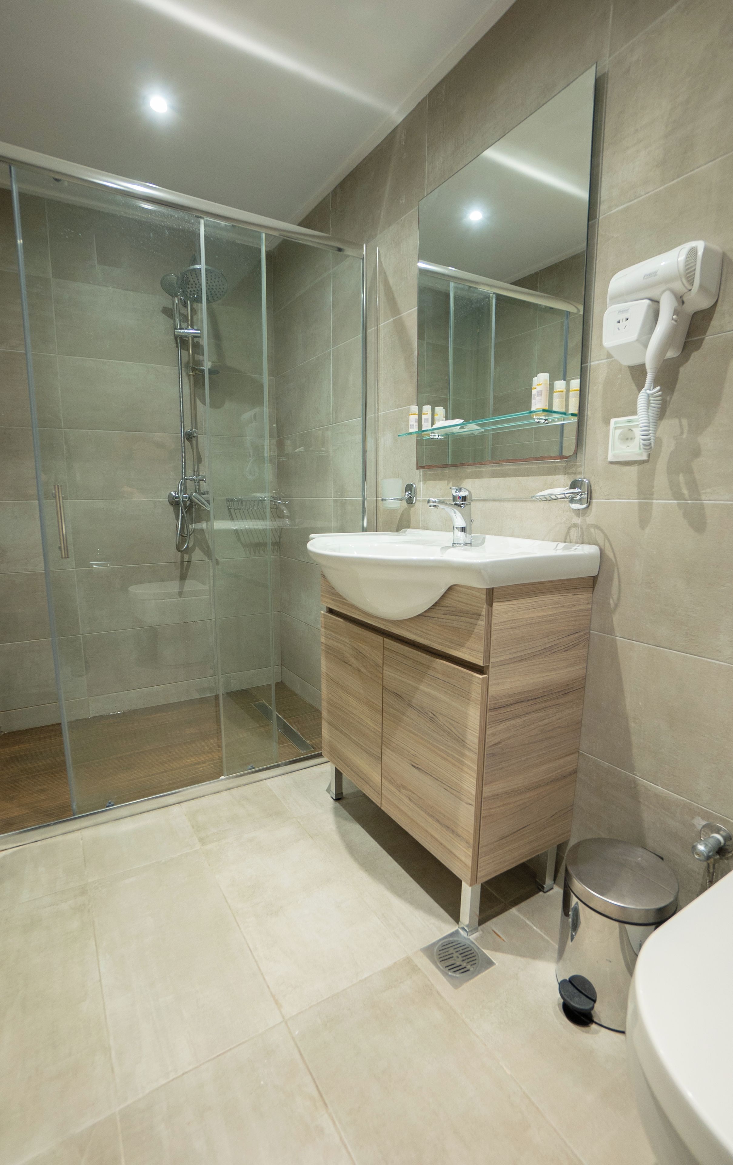 Een moderne badkamer met een douchecabine van glas, een houten wastafelmeubel en een ingebouwde haardroger.