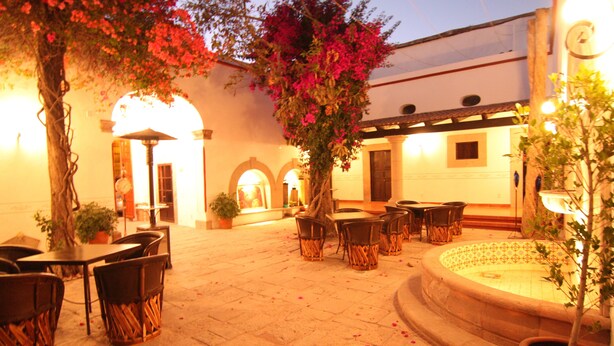 An outdoor patio area with stone flooring, tables, chairs, and a fountain. - Hotel Villa del Villar (Querétaro)