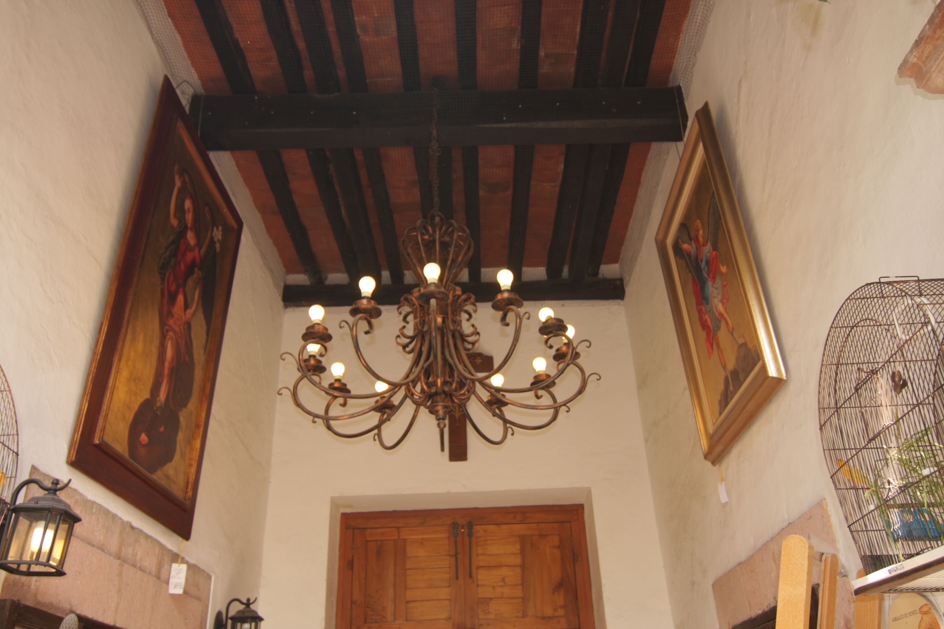 A room with a wooden door, a chandelier, and two framed paintings on the walls.