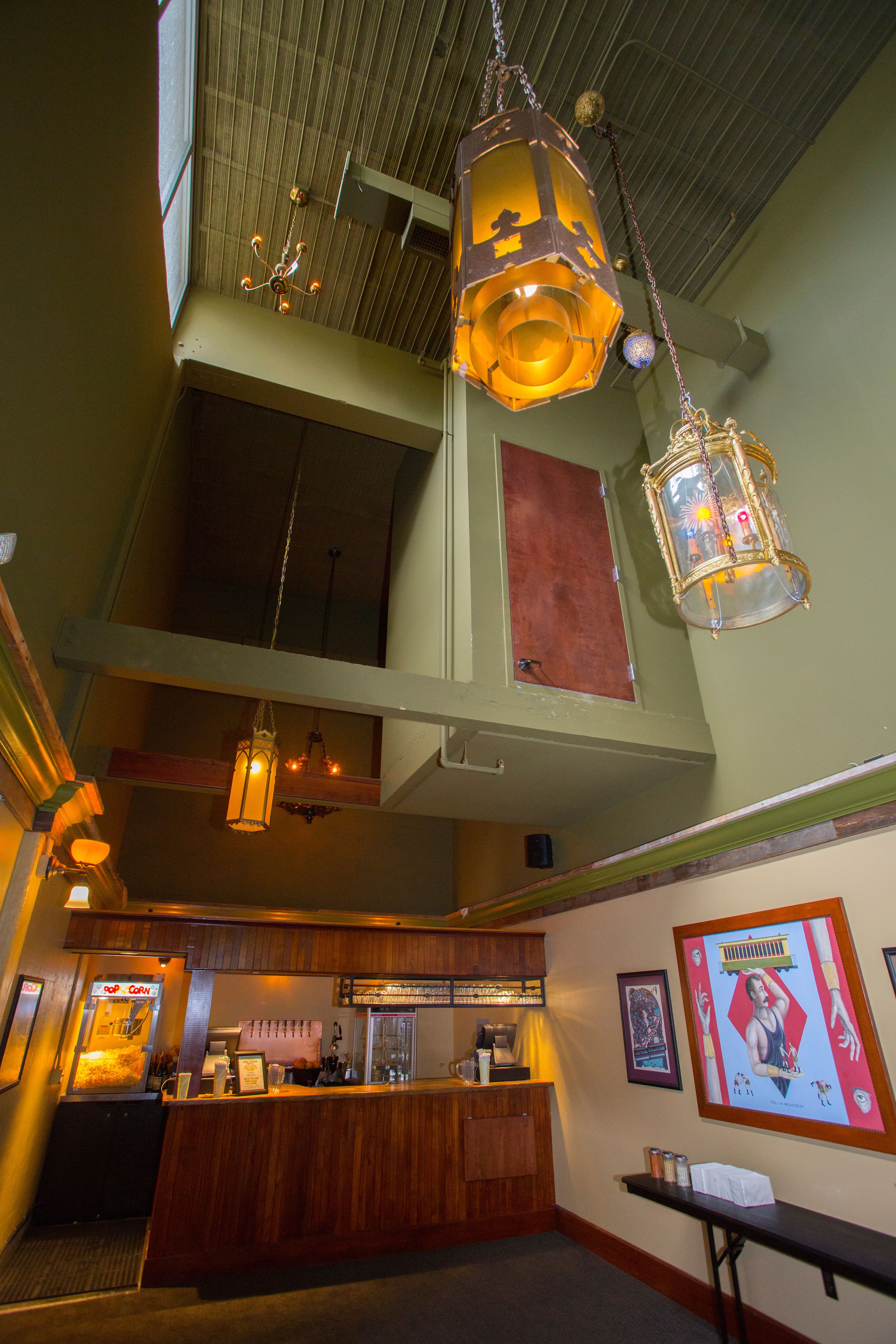 A high-ceilinged lobby with hanging lanterns, a reception desk, and artwork on the walls.