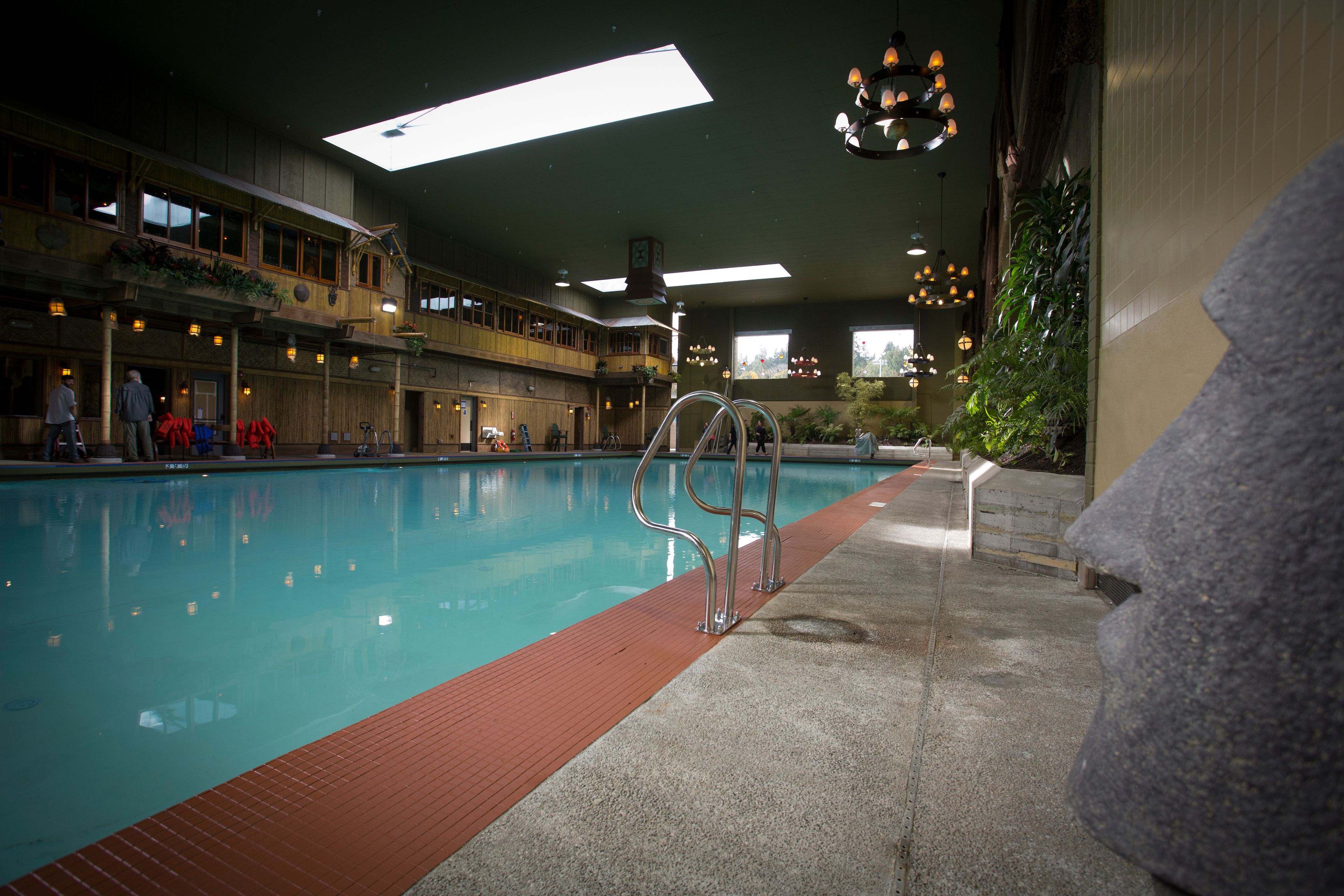 An indoor swimming pool with a red safety strip, metal handrails, and a stone wall on one side.