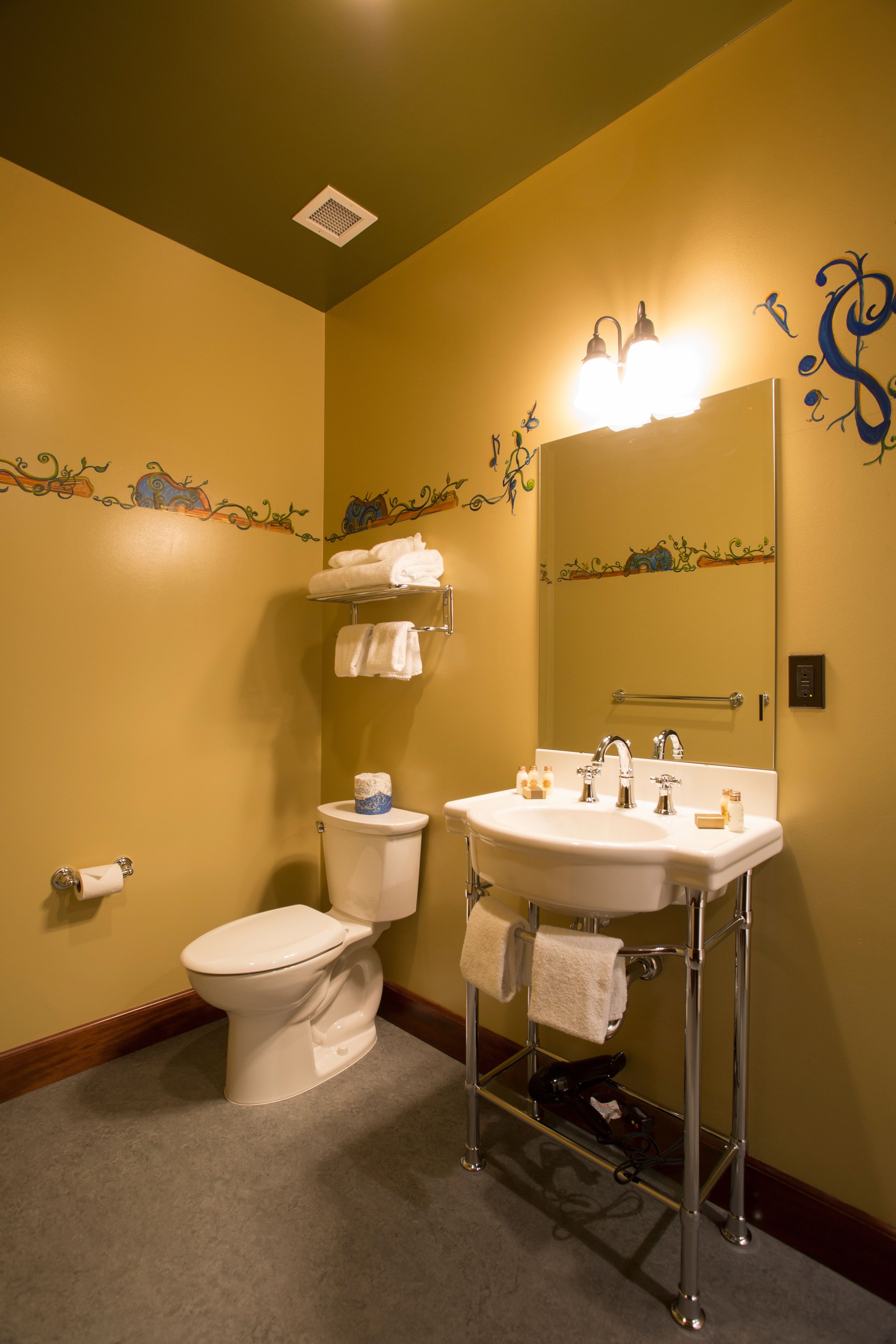 Une salle de bain avec des toilettes, un lavabo et un miroir. Il y a des serviettes accrochées au mur et une étagère au-dessus des toilettes.