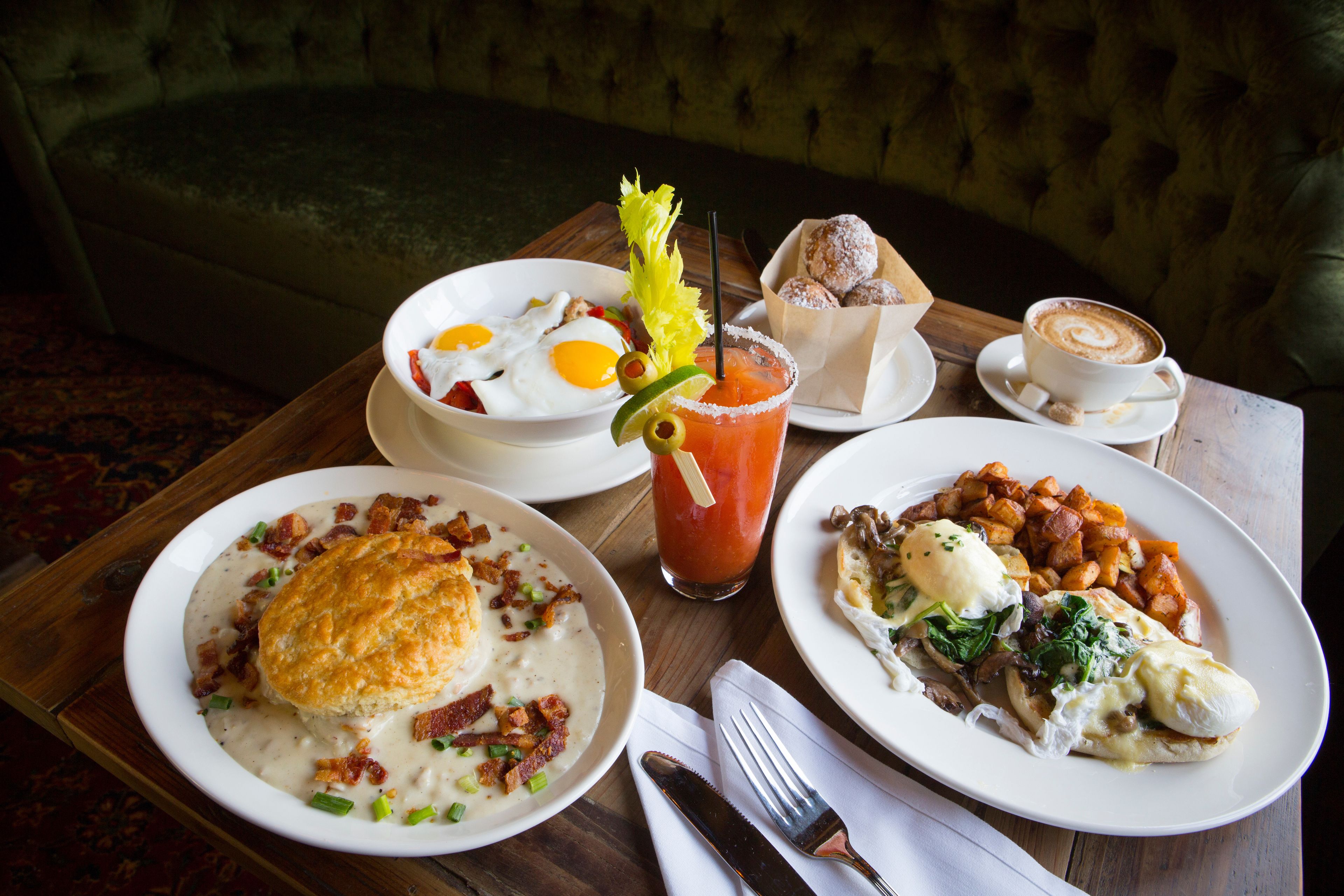 A breakfast table with various dishes including eggs, bacon, biscuits, and a Bloody Mary.