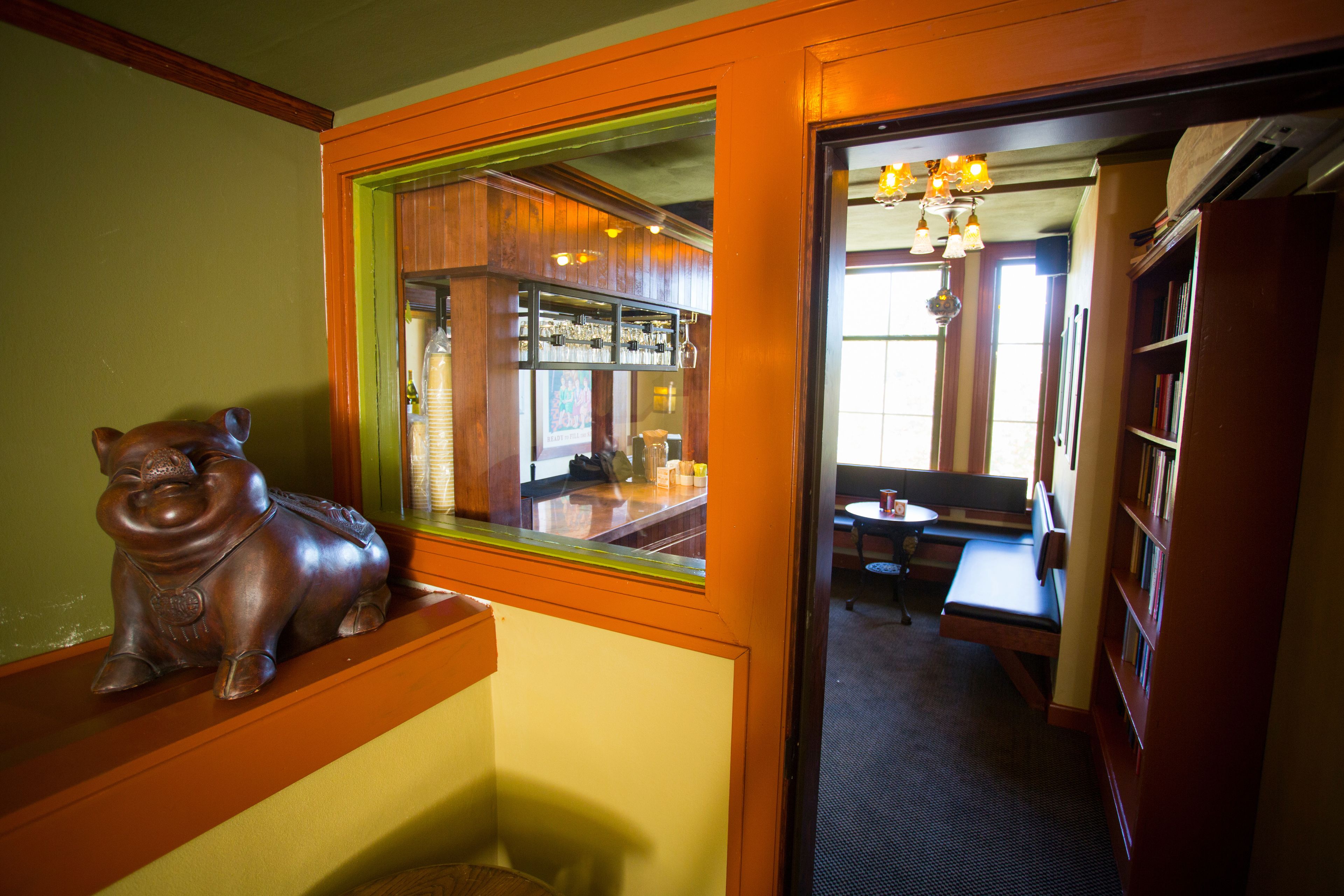 A corner of a room with a wooden piggy bank, a bar area with shelves of bottles, and a seating area with a table and chairs.