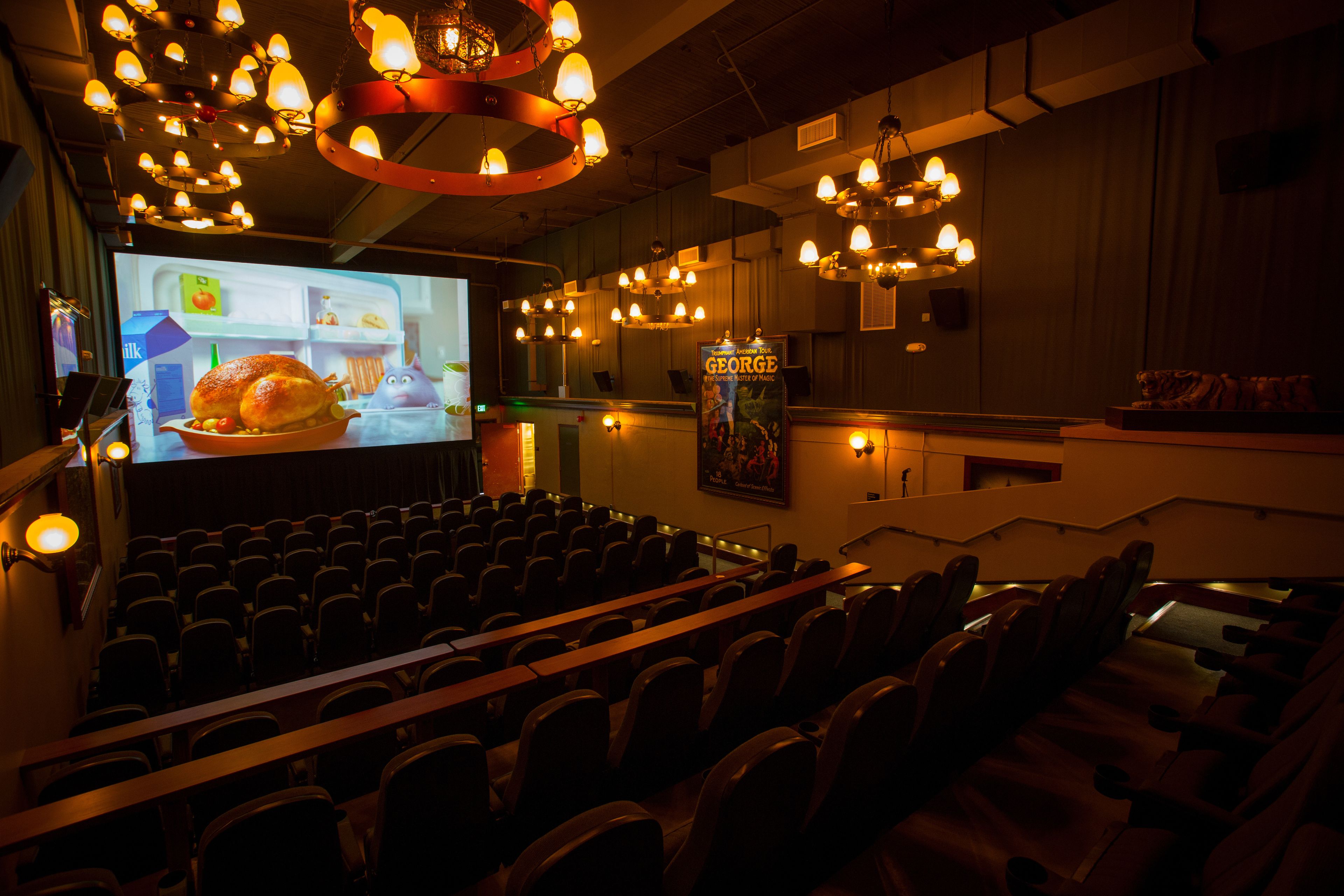 A theater with rows of seats, a large screen, and multiple chandeliers.