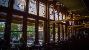 A restaurant with large stained glass windows, wooden beams, and hanging lanterns. - McMenamins Anderson School (Bothell)
