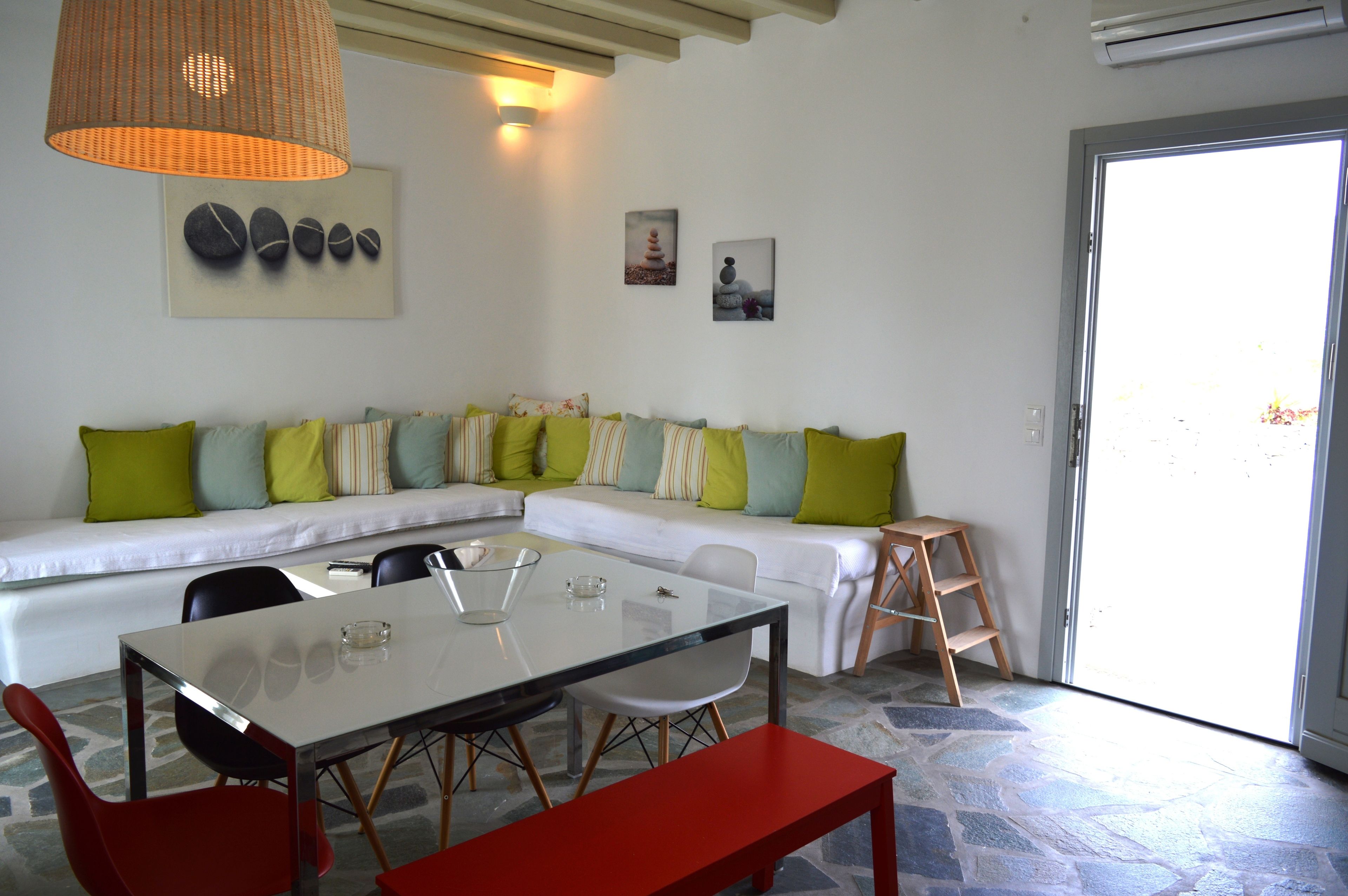 Una sala moderna con una mesa de comedor de vidrio, sillas rojas, un sofá blanco con cojines verde y a rayas, y una escalera de madera.