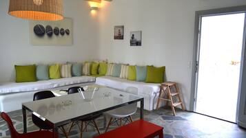 Una sala moderna con una mesa de comedor de vidrio, sillas rojas, un sofá blanco con cojines verde y a rayas, y una escalera de madera.