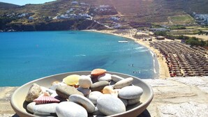 Vista costera con playa, una hilera de cabañas de playa y un cuenco con conchas marinas en primer plano.