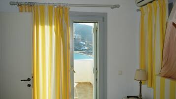 Una habitación con puerta a un balcón que ofrece vistas a la playa y las montañas.