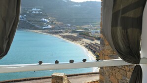 Vista costera desde un balcón con barandilla, que da a una playa con sombrillas y un muro de piedra.