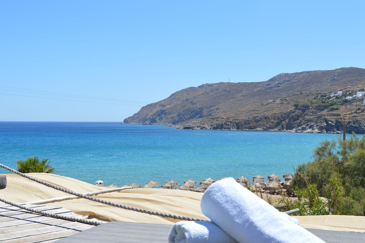 A beach view with a clear sky, a sandy area with a rope barrier, and a white building in the distance.