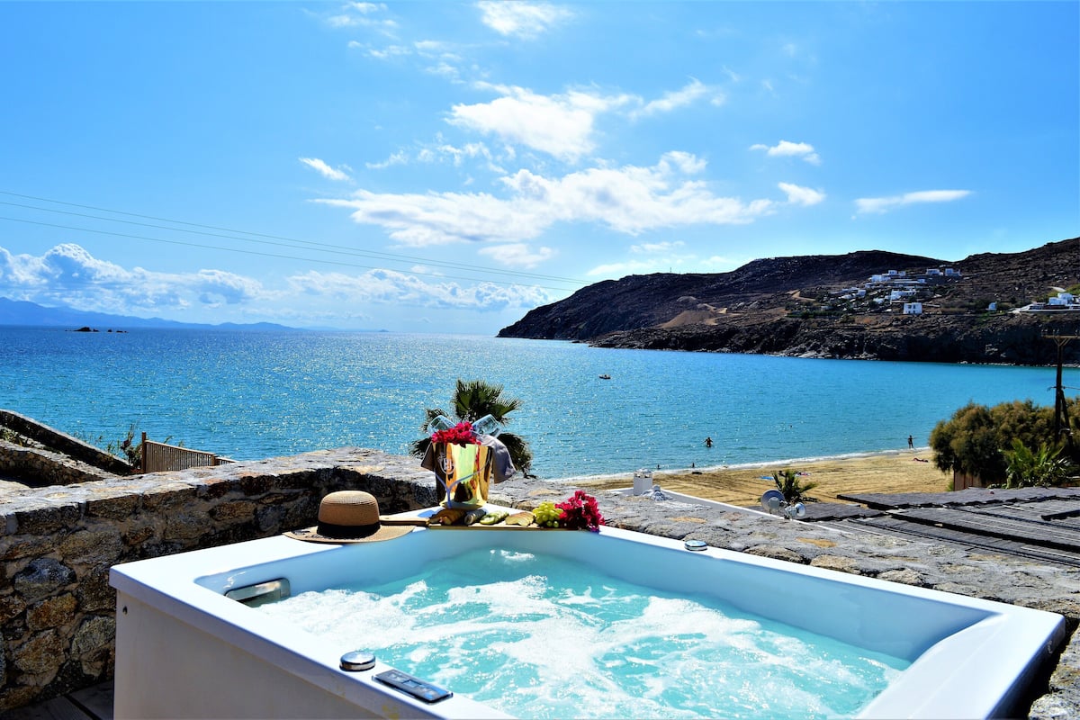 A stone-walled infinity pool with a view of the sea and a beach.