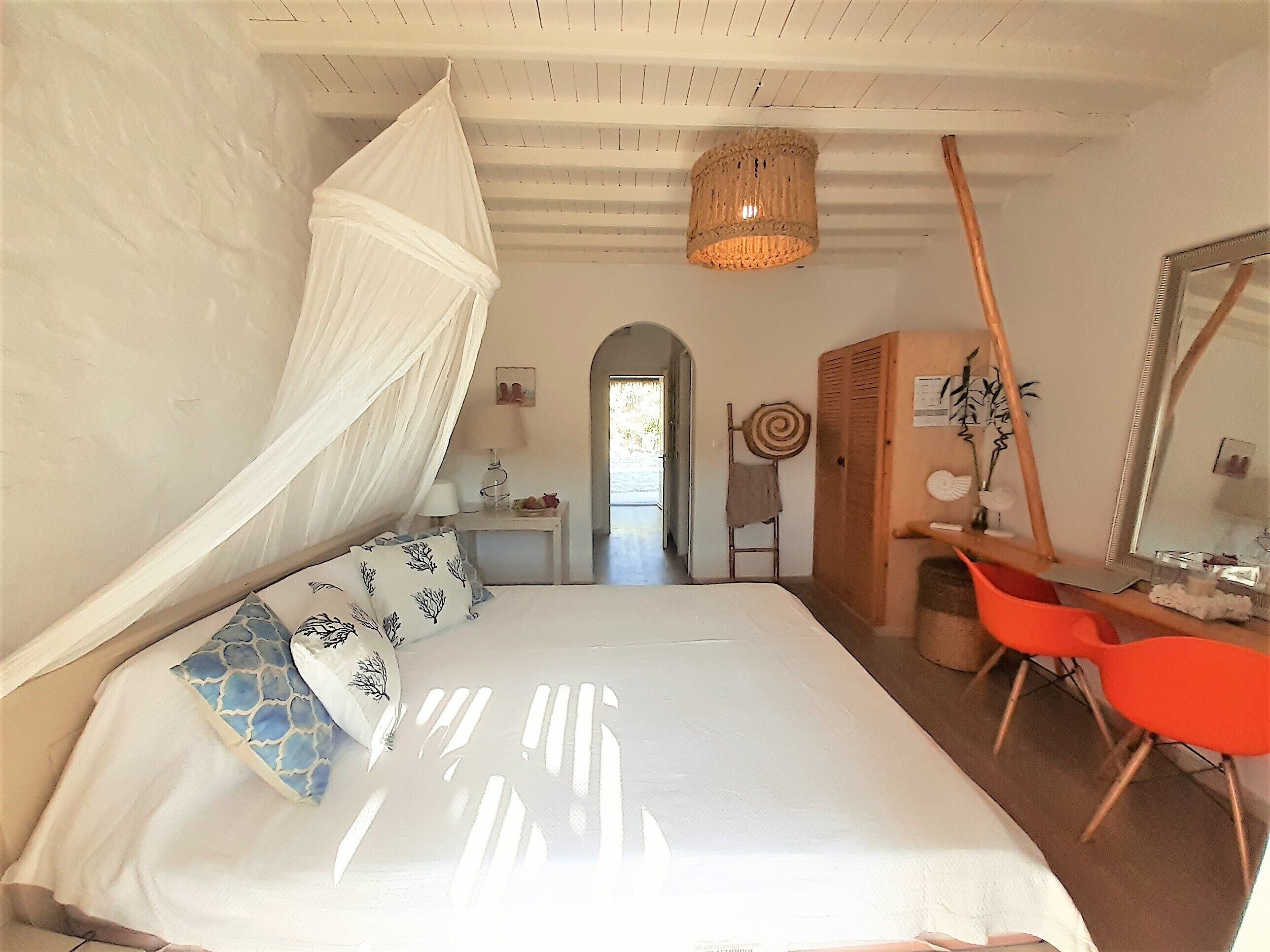 A bedroom with a canopy bed, a desk, a chair, a mirror, and a hanging light fixture.