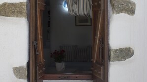 A small, rustic wooden door with a curtain, set in a white wall with stone patches. - Sourmeli Garden (Mykonos)