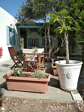 An outdoor seating area with a table and chairs, surrounded by potted plants and a large planter.