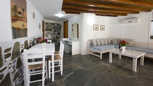 A room with a stone wall, a white desk, a white chair, a blue sofa, and a white coffee table. - Sourmeli Garden (Mykonos)