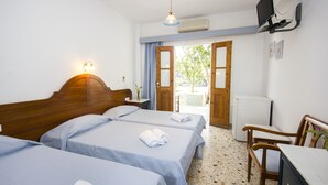 A hotel room with two beds, a desk, a chair, a TV, and a door leading to an outdoor area. - Sourmeli Garden (Mykonos)