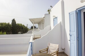 A white building with blue doors and windows, a covered outdoor seating area, and a staircase leading to a balcony.