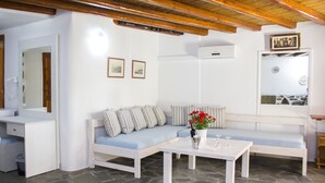A modern living room with a stone floor, a white sofa with striped cushions, a white coffee table with a vase of flowers, and a wooden ceiling. - Sourmeli Garden (Mykonos)