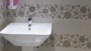 Un baño con un lavamanos blanco, un espejo con marco de madera y papel tapiz estampado con motivos florales.
