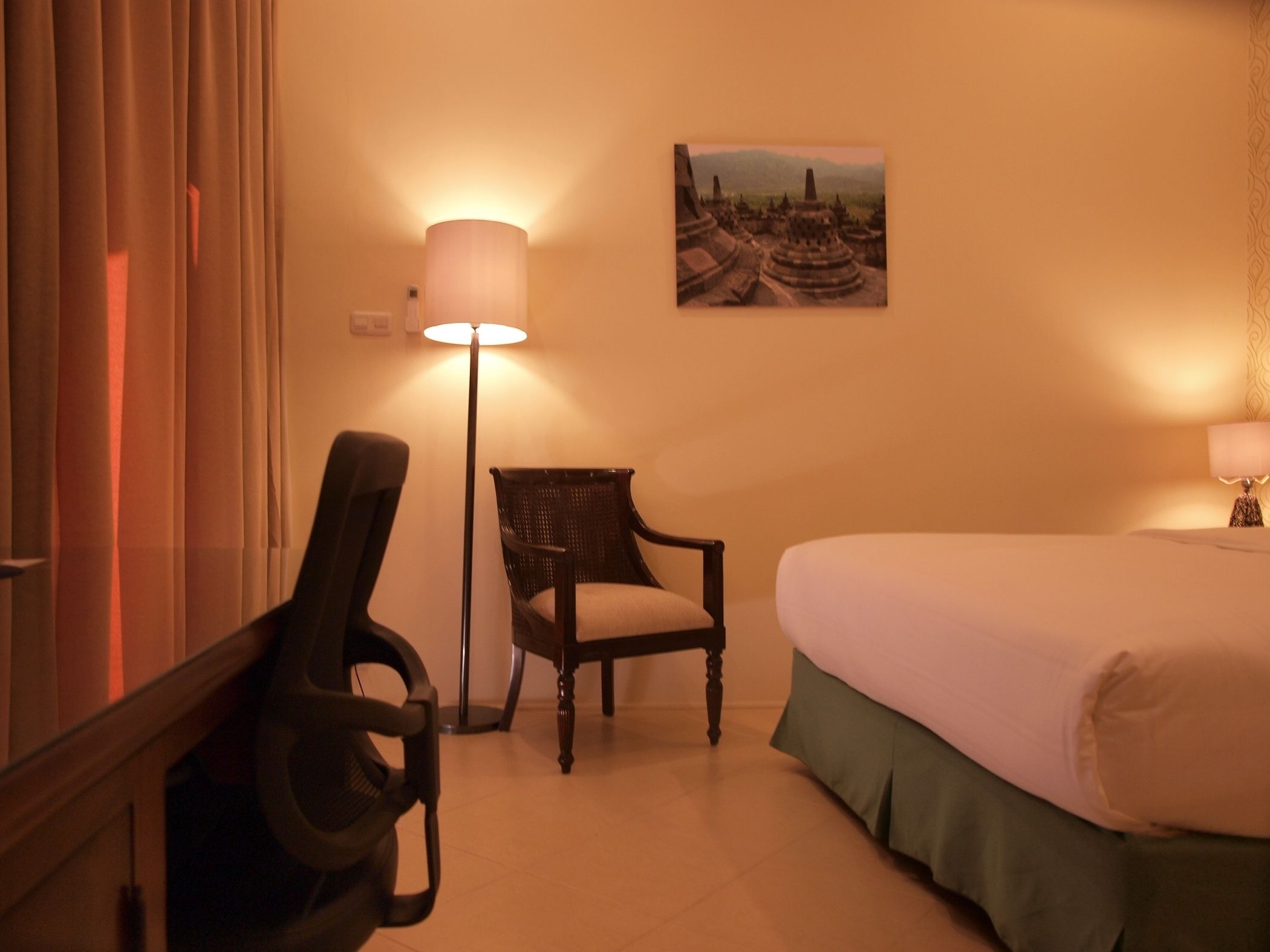 A hotel room with a bed, a chair, a desk, and a lamp.