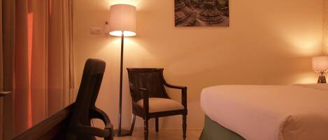 A hotel room with a bed, a chair, a desk, and a lamp.
