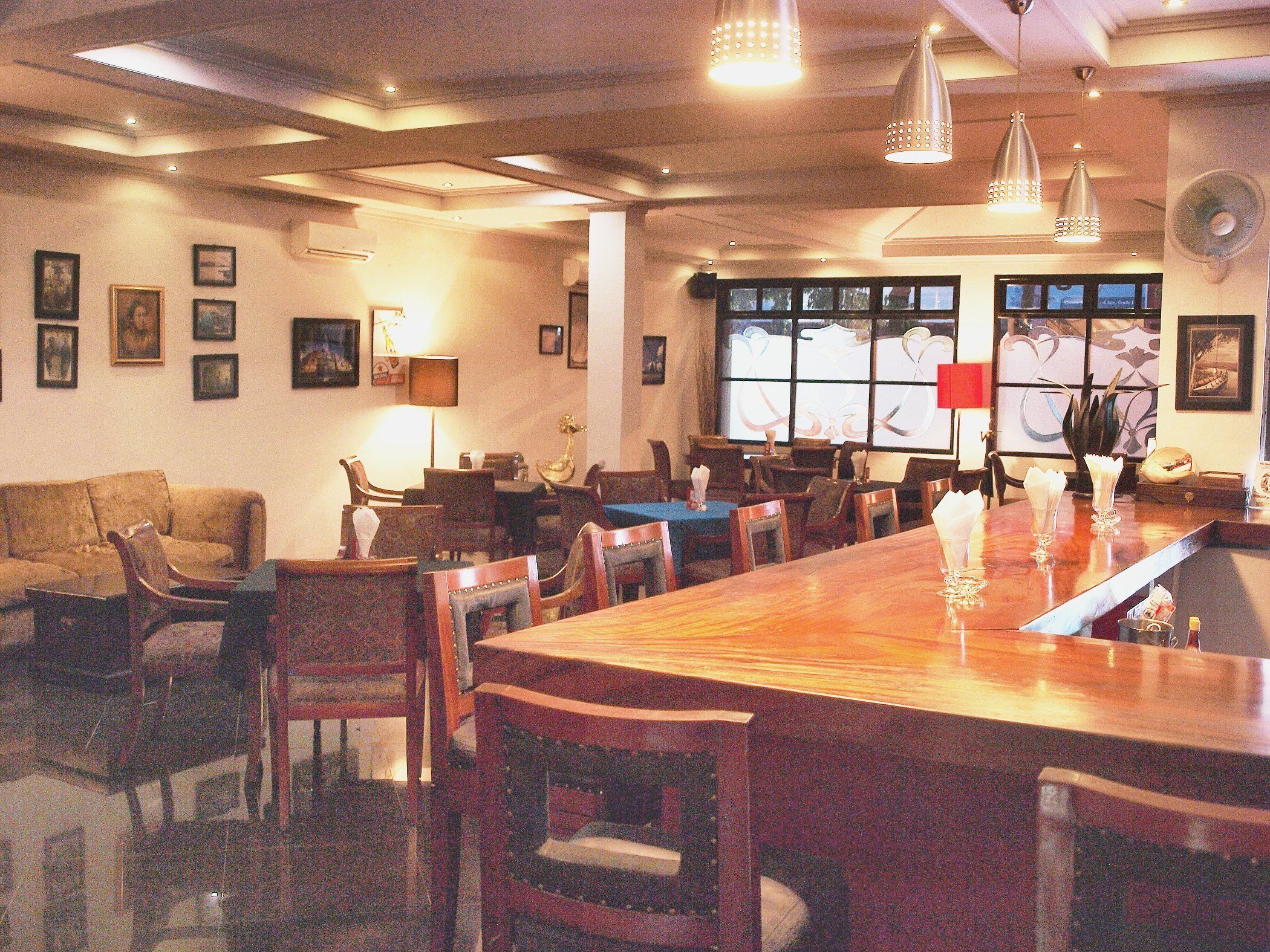 A restaurant with a long wooden table, multiple chairs, and pendant lighting.