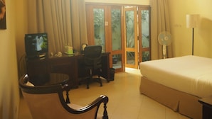 Habitación de hotel con cama, escritorio con computadora, silla, bote de basura y ventana con cortinas.