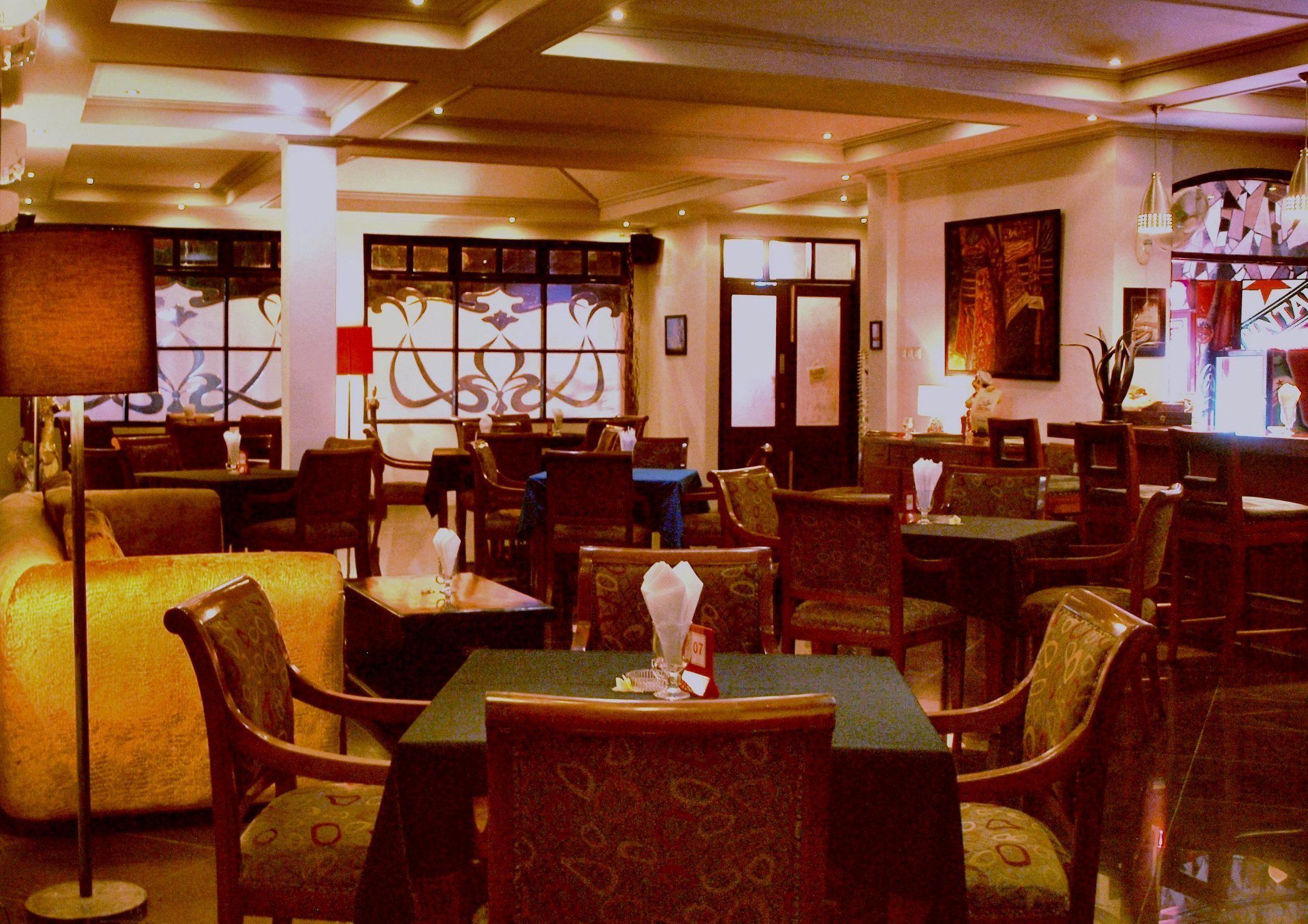 A restaurant with multiple tables and chairs, a patterned floor, and a large window with decorative glass.