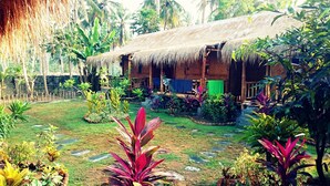 A rustic thatched-roof house with a garden in front. - Same Same - Bungalows - Hostel (Kuta)