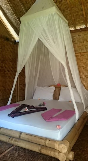 A bed with a white canopy, wooden headboard, and a woven floor. - Same Same - Bungalows - Hostel (Kuta)