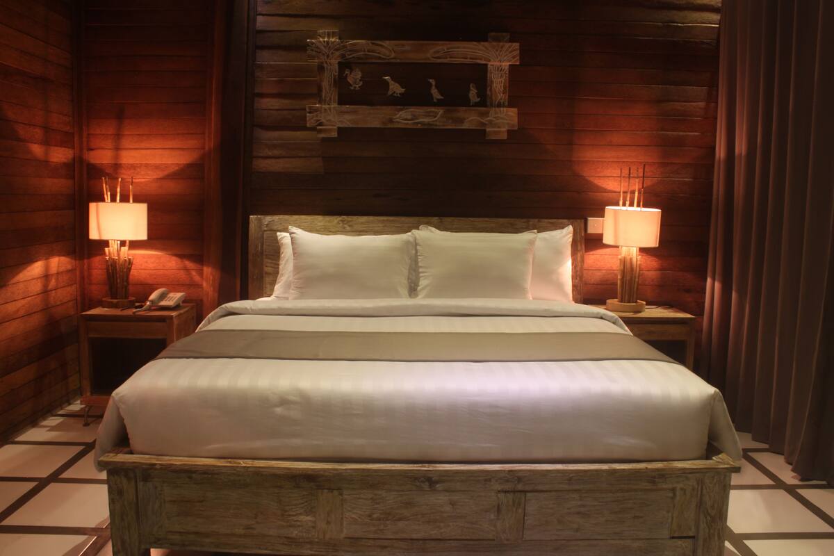 A wooden-framed bed with white linens, two bedside lamps, and a wall-mounted artwork above the bed.
