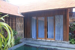 Une maison en bois avec un toit en tuiles, une piscine et une clôture en bambou.