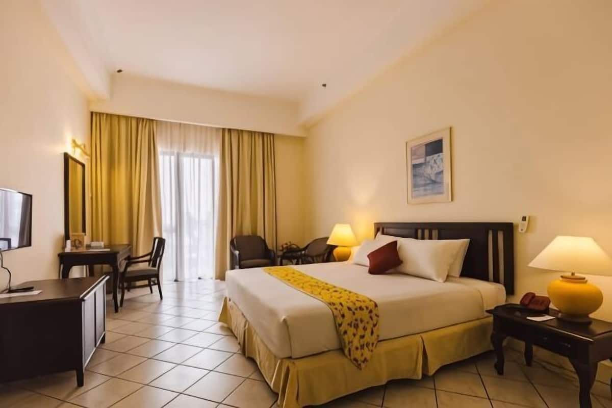 A hotel room with a bed, bedside lamps, a desk, a chair, and a television.