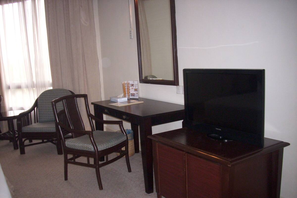 A hotel room with a wooden desk, two chairs, a television, and a mirror.
