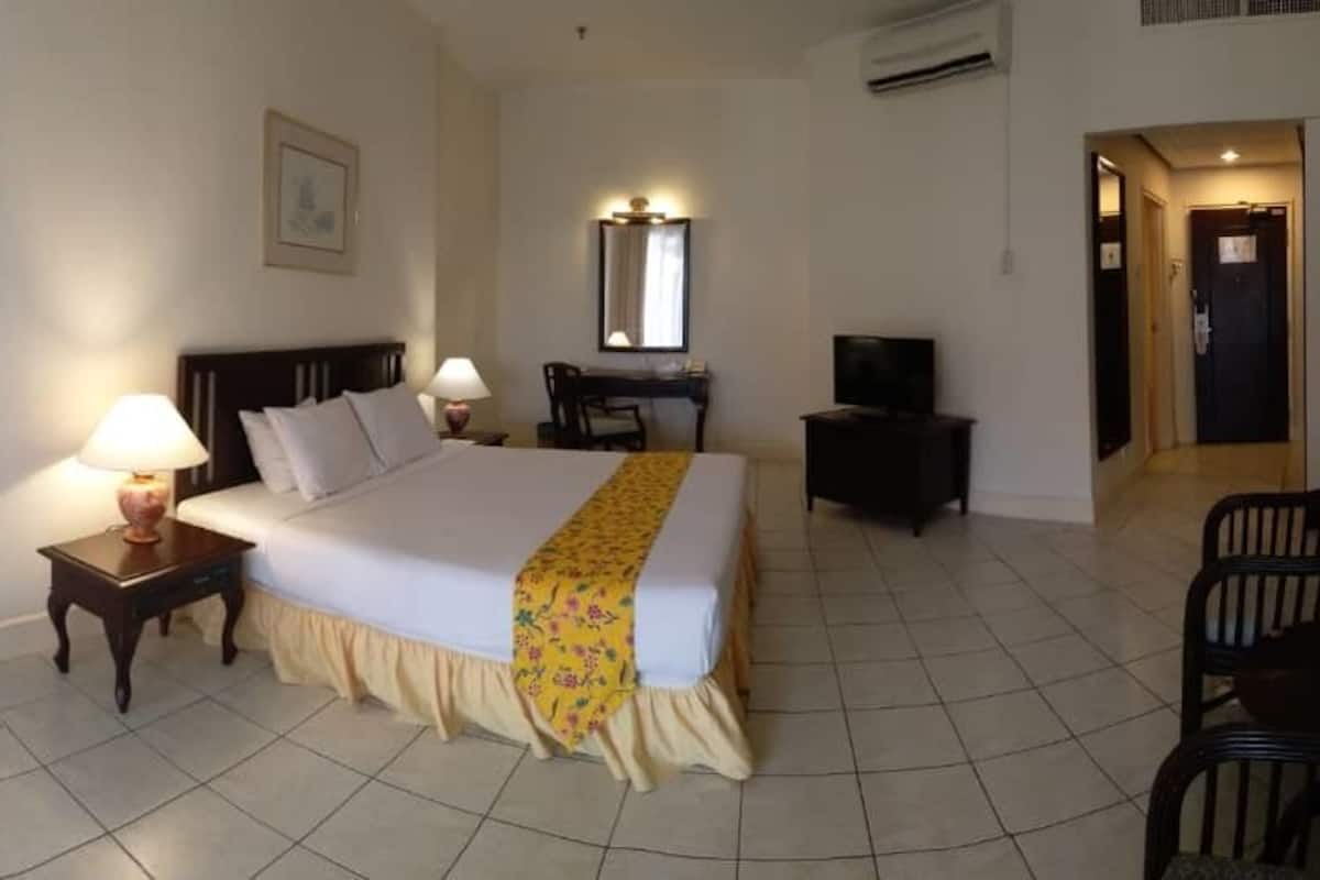 A hotel room with a bed, bedside lamps, a desk, a chair, and a television.