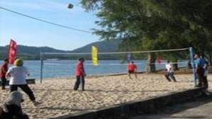Ein Beachvolleyballspiel auf einem Sandplatz mit Blick auf das Meer und die Berge im Hintergrund.