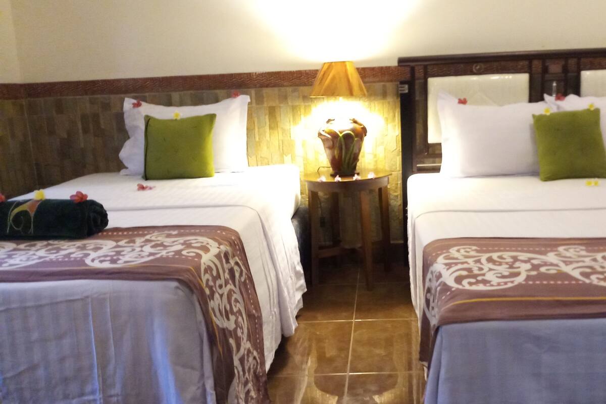 A hotel room with two beds, a nightstand with a lamp, and a tiled floor.