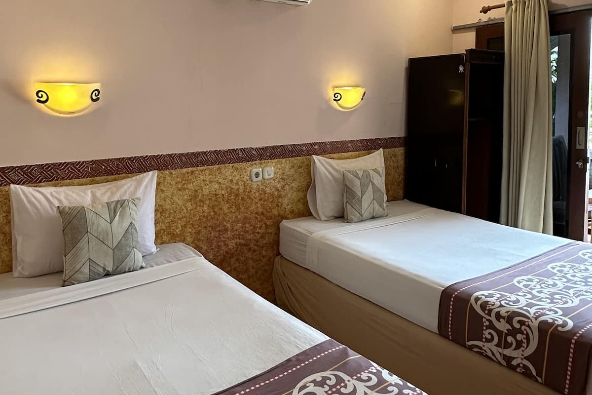 A hotel room with two beds, a wall-mounted air conditioner, and two wall sconces.